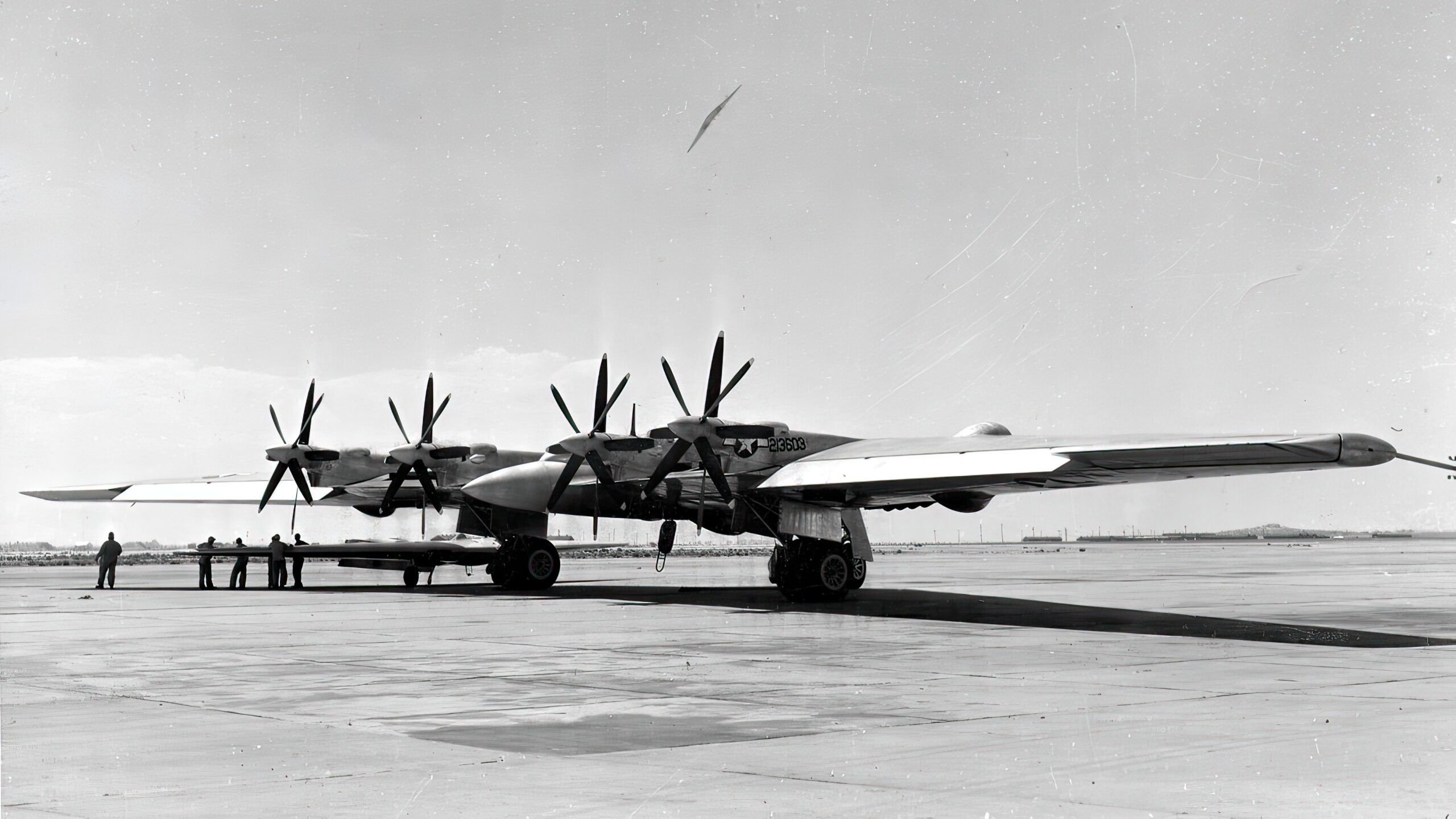 An XB-35 serial number 42-13603 on the ramp with it's ground crew with another shown flying above it