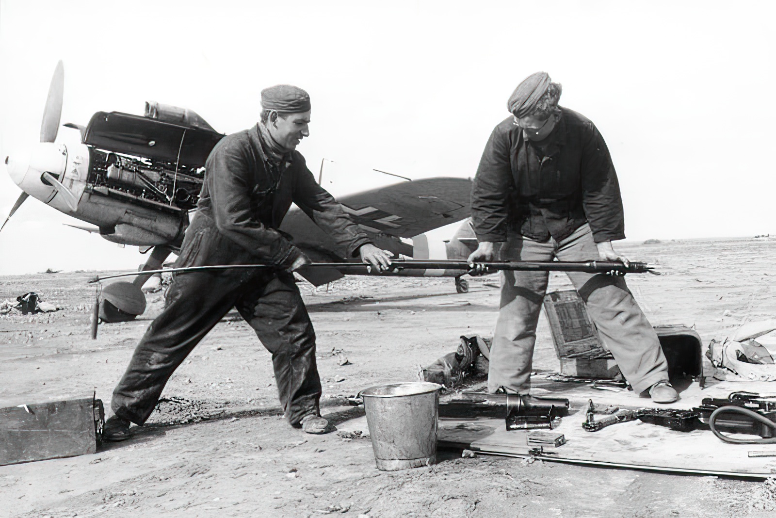 Marseille's service men, Hoffmann (left) and Berger, cleaning the bore of one of the cannons of a Bf 109. "Yellow 14" W.Nr. 8673 can be seen in the background