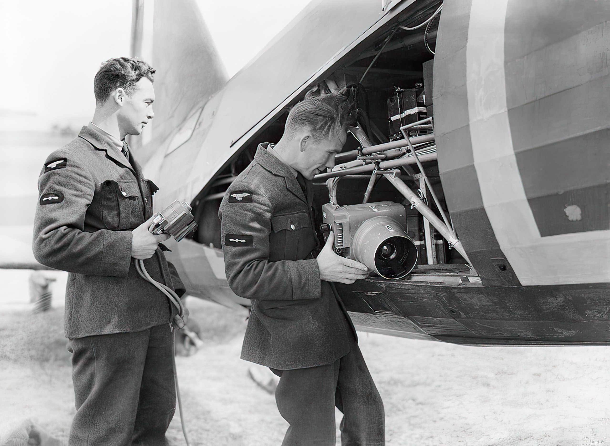 Groundcrew installing camera equipment into a Westland Lysander Mark II of No. 225 Squadron at RAF Tilshead, Wiltshire. The airman on the right loads a Type F.24 aerial camera into its position in the aircraft, while the airman on the left holds the camera motor unit